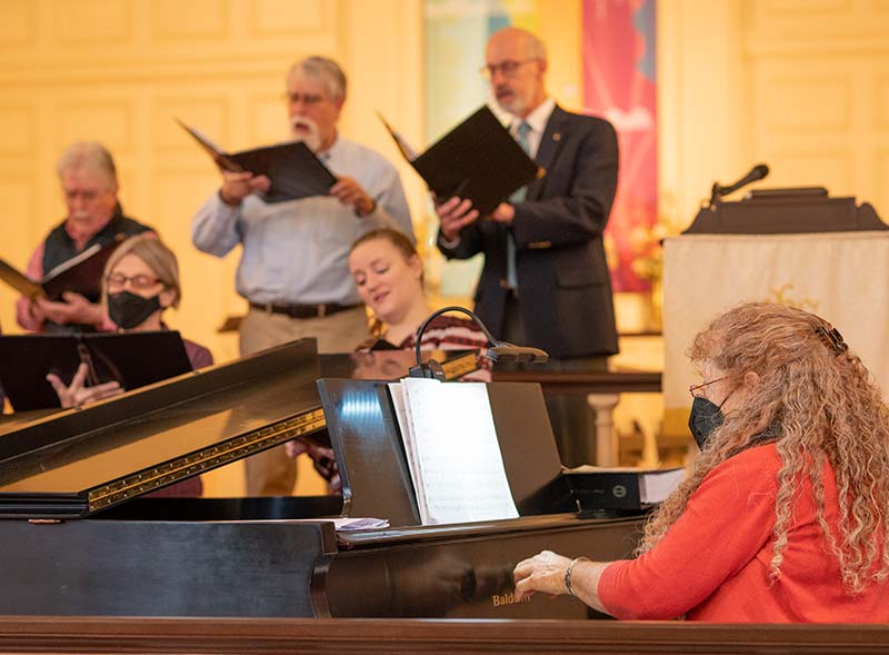 Choir Director Lynn Salmonsen plays piano with East Church choir in background